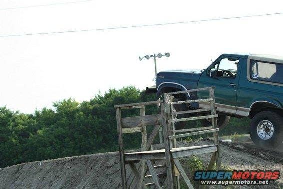 Green Ford Bronco on a dirt ramp, with a wooden structure in the foreground