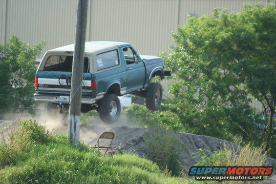 Ford Bronco mid-air over a dirt jump, kicking up dust
