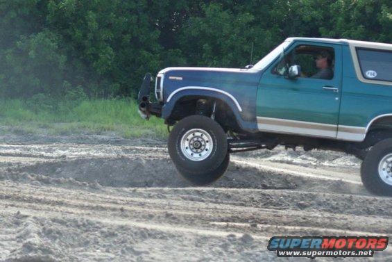 Green Ford Bronco with lifted suspension driving on dirt mounds
