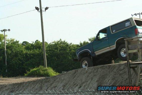 Green and tan Ford Bronco on a dirt ramp, right front tire elevated