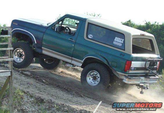 Green and tan Ford Bronco climbing a dirt hill, front wheel off the ground