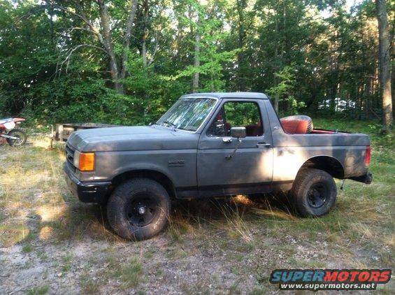 Gray 1987 Ford Bronco parked on grassy ground with trees in background