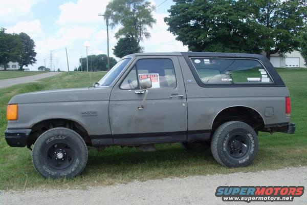 1987 Ford Bronco parked on grass with a 'For Sale' sign in the window
