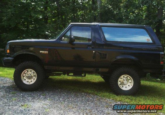 Black Ford Bronco SUV, side view, lifted suspension, aftermarket wheels, parked on gravel and grass