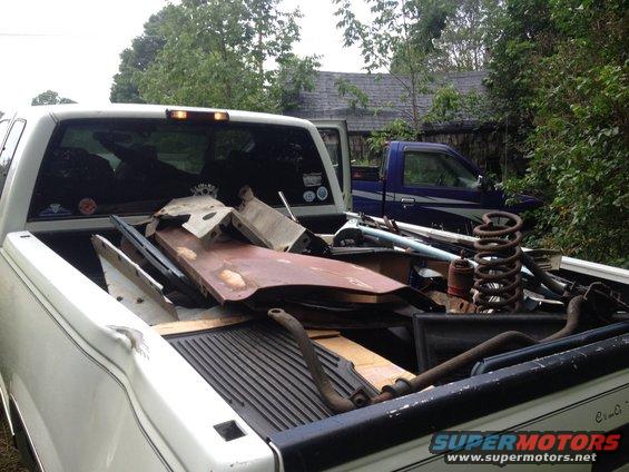 White pickup truck bed loaded with scrap metal and car parts, blue pickup truck in background
