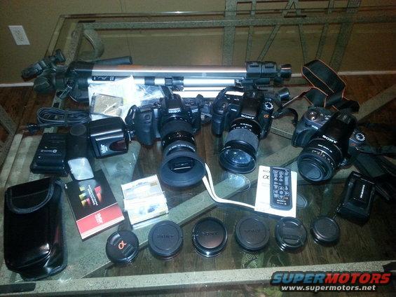 Camera equipment including tripods, cameras, lenses, and accessories on a glass table