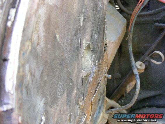 Close-up of a rusty, dented metal panel with exposed wires and a bolt