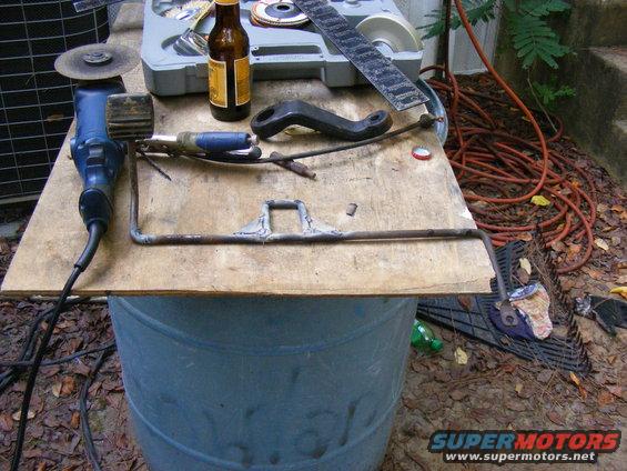 Metal bracket, grinder, beer bottle, and tools on a wooden surface over a blue barrel