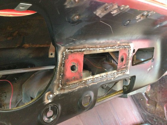 Car dashboard with welded metal patch over radio opening, red undercoating visible