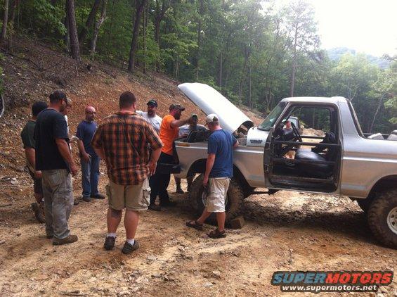 Silver 1989 Ford Bronco with hood open, surrounded by people on a dirt road