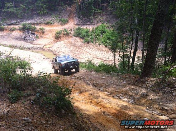 Green 1989 Ford Bronco driving on a dirt trail