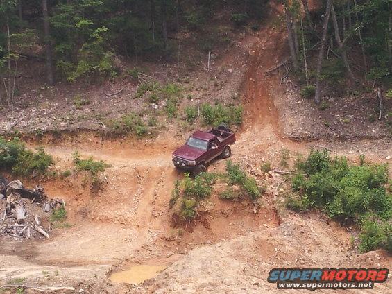 Maroon pickup truck driving down a steep dirt hill with trees on either side