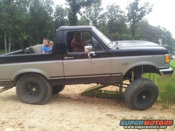 Side view of a lifted, two-tone pickup truck with people in the cab and bed