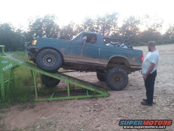 Green Ford Bronco with roll cage on a green ramp, front right tire elevated