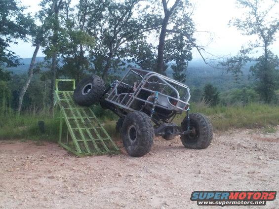 Custom tube-frame buggy with large tires on a green metal ramp, outdoors