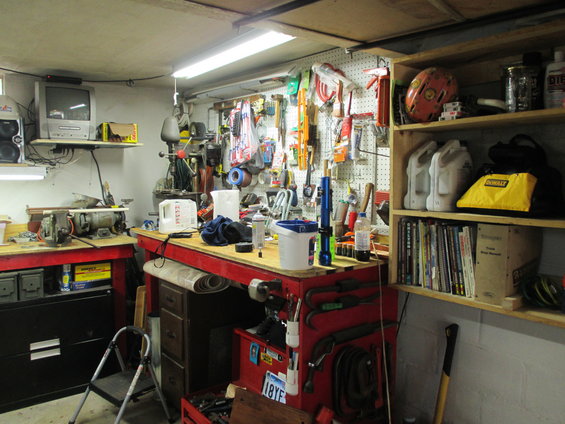 Workshop with red tool chests, pegboard full of tools, shelves with oil cans and books, and a vintage TV