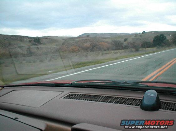 Dashboard of a red car with a black GPS device and a view of a rural road