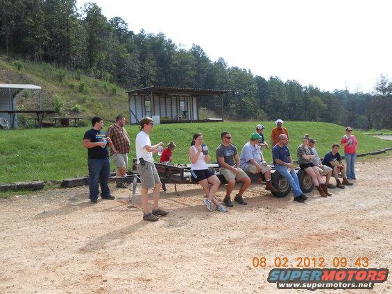 People sitting on a trailer with a building and trees in the background