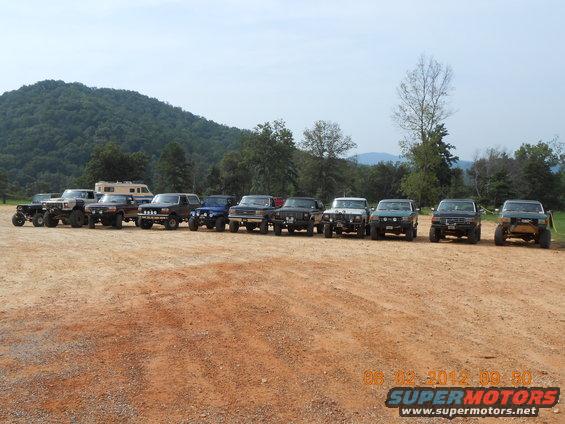Multiple off-road vehicles parked in a line on a dirt lot with trees and hills in the background. Timestamp 08-02-2012