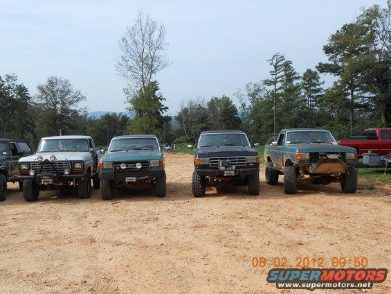 Four lifted trucks parked in a dirt lot