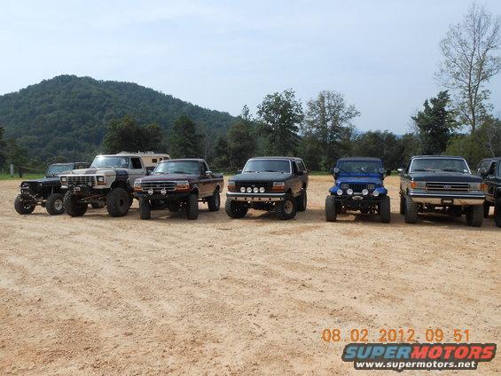 Dark blue 1992 Ford Bronco with aftermarket lights parked in a line of off-road vehicles