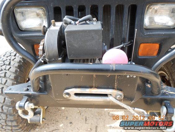 Jeep Wrangler front end with winch, aftermarket bumper, and large tires. Grille shows vertical slots