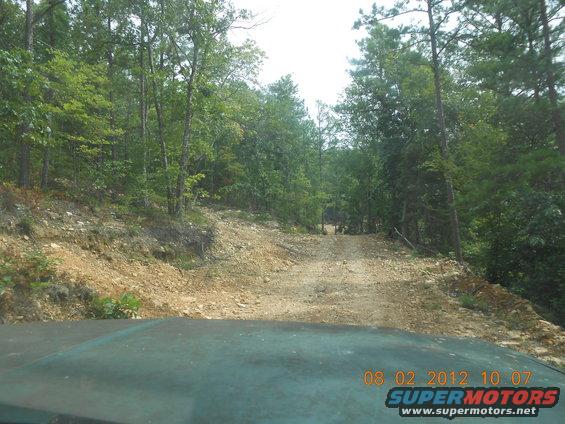 view from inside a vehicle looking down a rough dirt road in a wooded area. Timestamp reads 08 02 2012