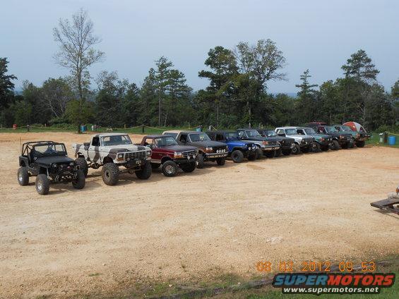 Line of lifted off-road trucks and SUVs parked on dirt lot
