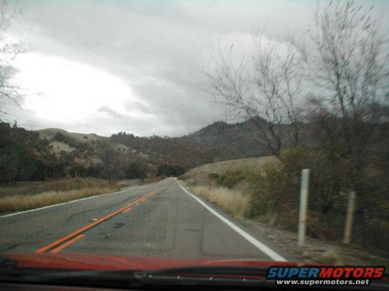 View of a two-lane road winding through rolling hills under a cloudy sky