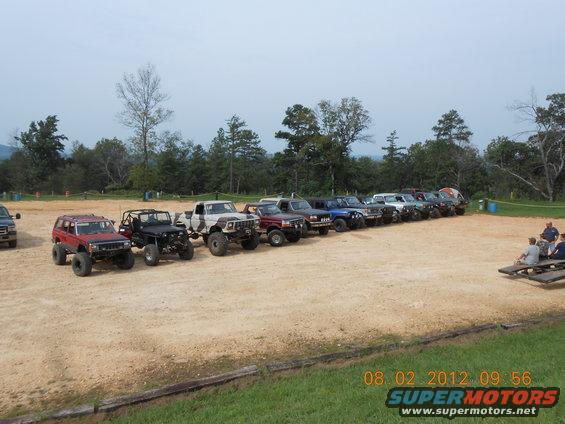 Line of modified off-road SUVs and trucks parked on dirt, side view