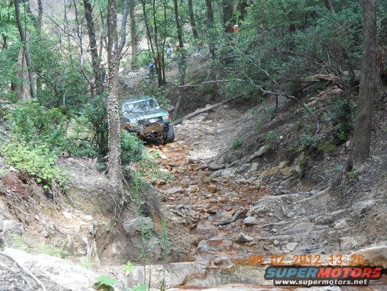 Green off-road vehicle navigating a steep, rocky trail in a forest