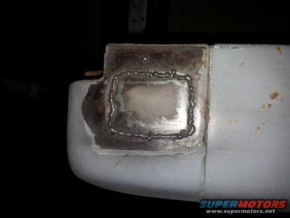Welded metal patch on a light-colored vehicle body, showing rough weld beads and a ground metal surface