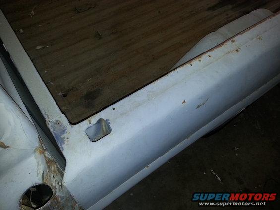 Close-up of a truck bed corner, showing wooden planks and a light blue painted metal side with some rust spots