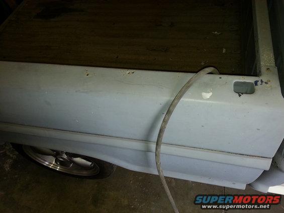 Light blue 1967 Ford F-100 truck bed side panel with a hose running across it and a chrome wheel visible
