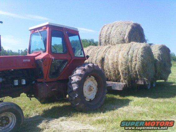 Red tractor with a cab, pulling a trailer loaded with round hay bales on a sunny day