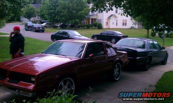 Maroon coupe with chrome wheels parked in driveway, other cars visible