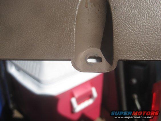Close-up of a tan interior trim piece with a hole for a clip. A red and white cooler is visible below