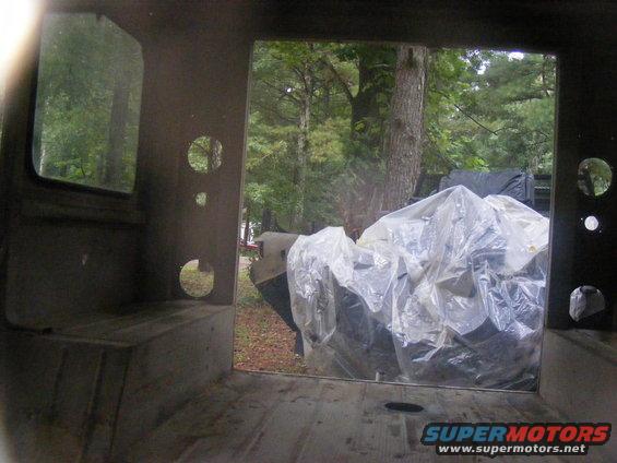 Looking out from inside a vehicle, trees and a covered object are visible outside