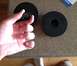 1996 Ford Bronco - A hand holds a black circular body mount part. Another identical part is visible on the counter.