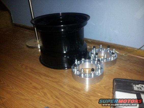Black wheel and two silver wheel adapters with studs on a wood floor