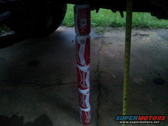Stack of Budweiser cans supporting the underside of a vehicle, with a tape measure next to it