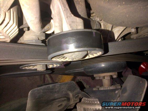 Close-up of engine belt tensioner and pulleys. Watermark says SUPERMOTORS.NET