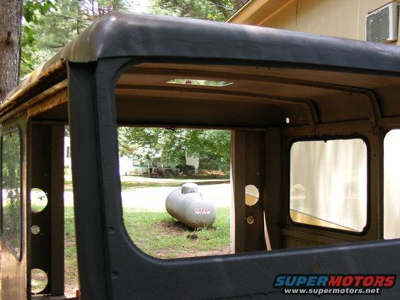 Interior of a dark-colored vehicle with large windows and an open doorway revealing a propane tank outside