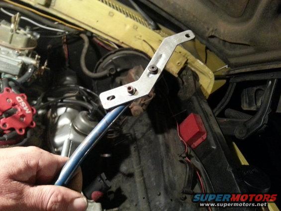 Hand holding blue metal rod near yellow engine bay with red MSD distributor
