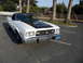 1973 Ford Ranchero - A white coupe utility with a black hood and vinyl roof is parked in a lot with palm trees.