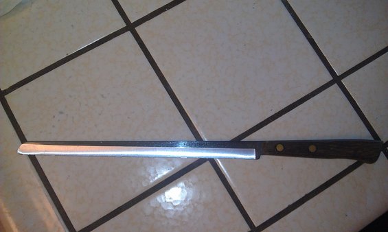Bread knife with serrated blade and dark wood handle with two brass rivets, lying on a tiled surface