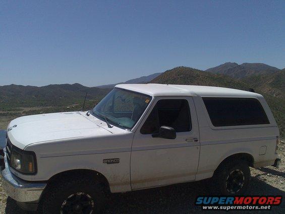 White Ford Bronco parked on a dirt road with hills in the background