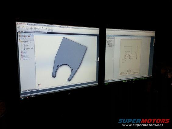 Photo of dual monitors showing a CAD bracket model and a dimensioned engineering drawing