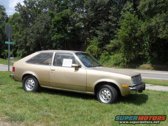 Gold hatchback car parked on grass, side view. Price tag in window