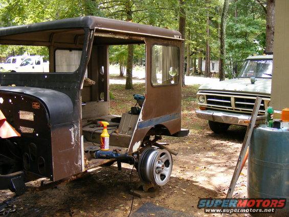 Rusty vehicle cab in foreground, light-colored truck in background